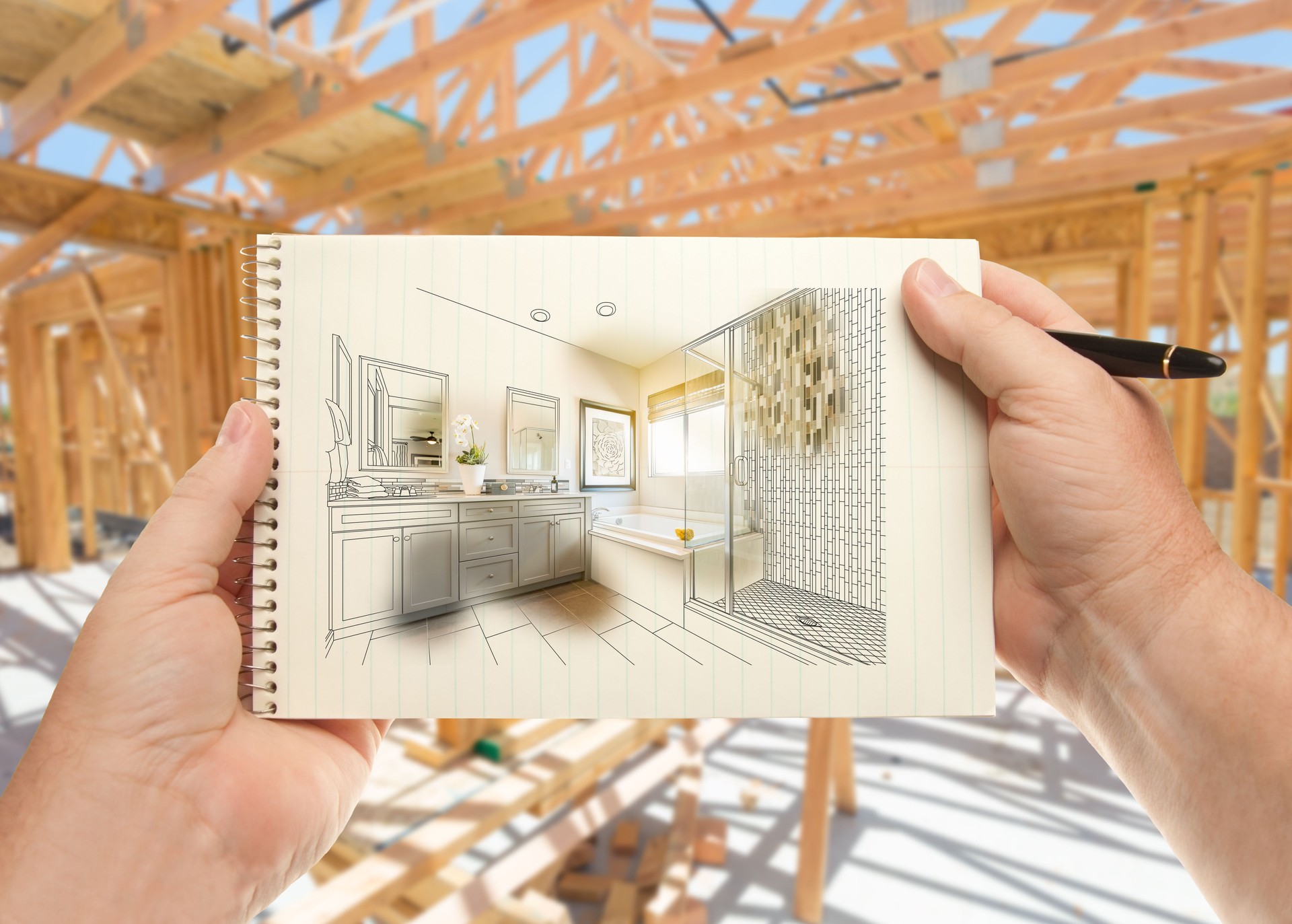 Hands Holding Pen and Pad of Paper with Bathroom Design Inside House Construction Framing.